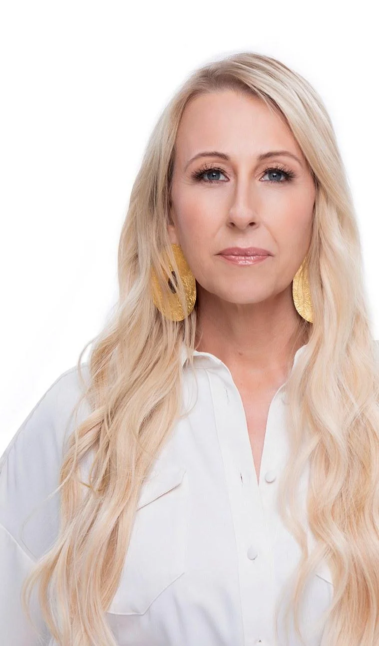 Professional portrait of a blonde woman in a white blouse with gold earrings against a white background.